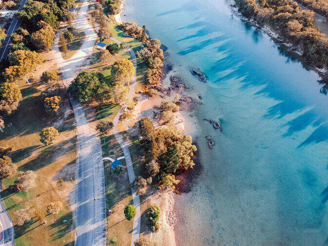 Aerial view of a sun-drenched riverbank with winding walking paths and golden foliage, showcasing the calm, nature-filled charm of the Tweed Coast during NSW winter.