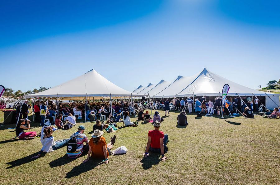 People gathered at large white tents during an outdoor festival under clear blue skies, enjoying one of the vibrant NSW events near Cabarita Beach.