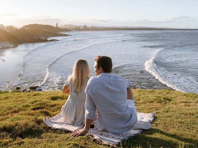 Things to do Cabarita Beach: couple sitting on a picnic rug overlooking the ocean and headland at sunrise
